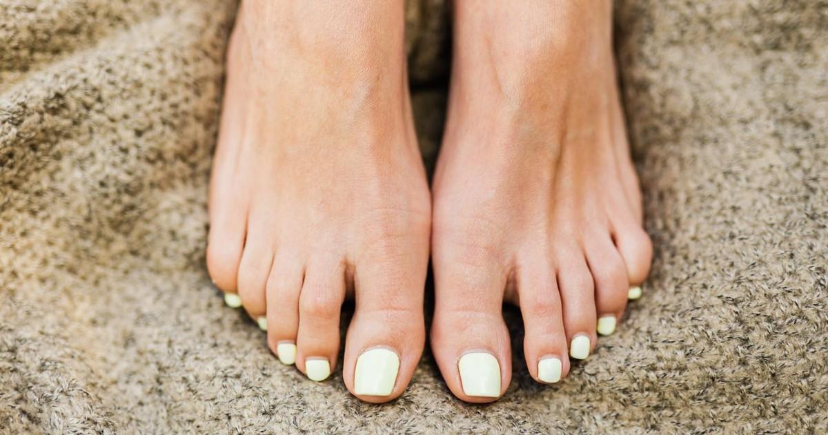 Gros plan de pieds féminins soignés aux ongles vernis vert clair sur une surface texturée